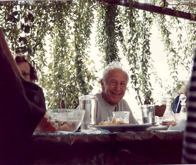 Alexander Lowen laughing at an outdoor table, greenery behind him
