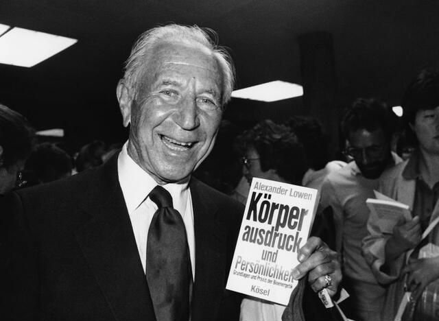 Alexander Lowen smiling as he holds a German edition of one of his books at a book event